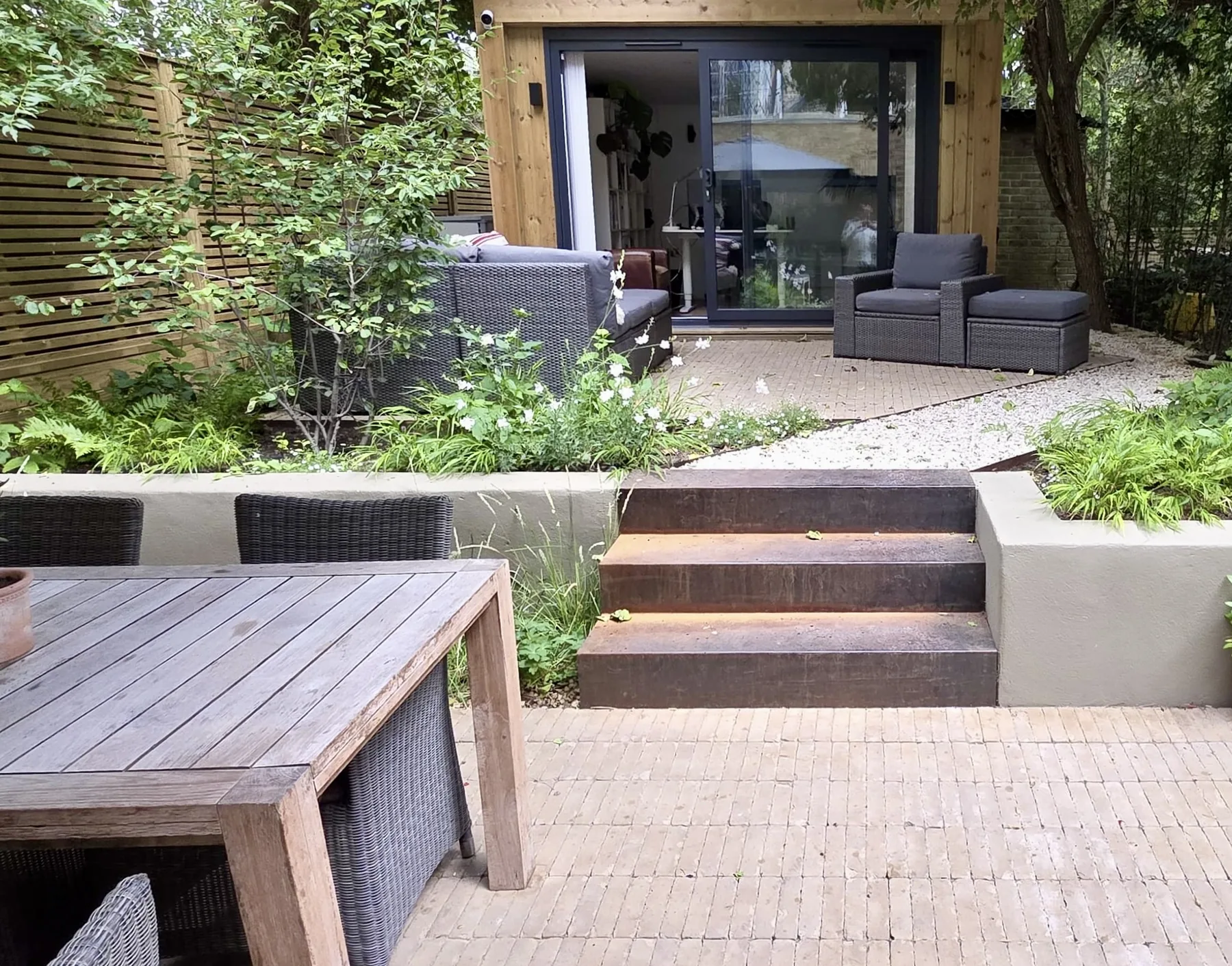 Corten steel steps between pale rendered retaining walls in a shady Brixton garden, with ferns, grasses and a gravel path